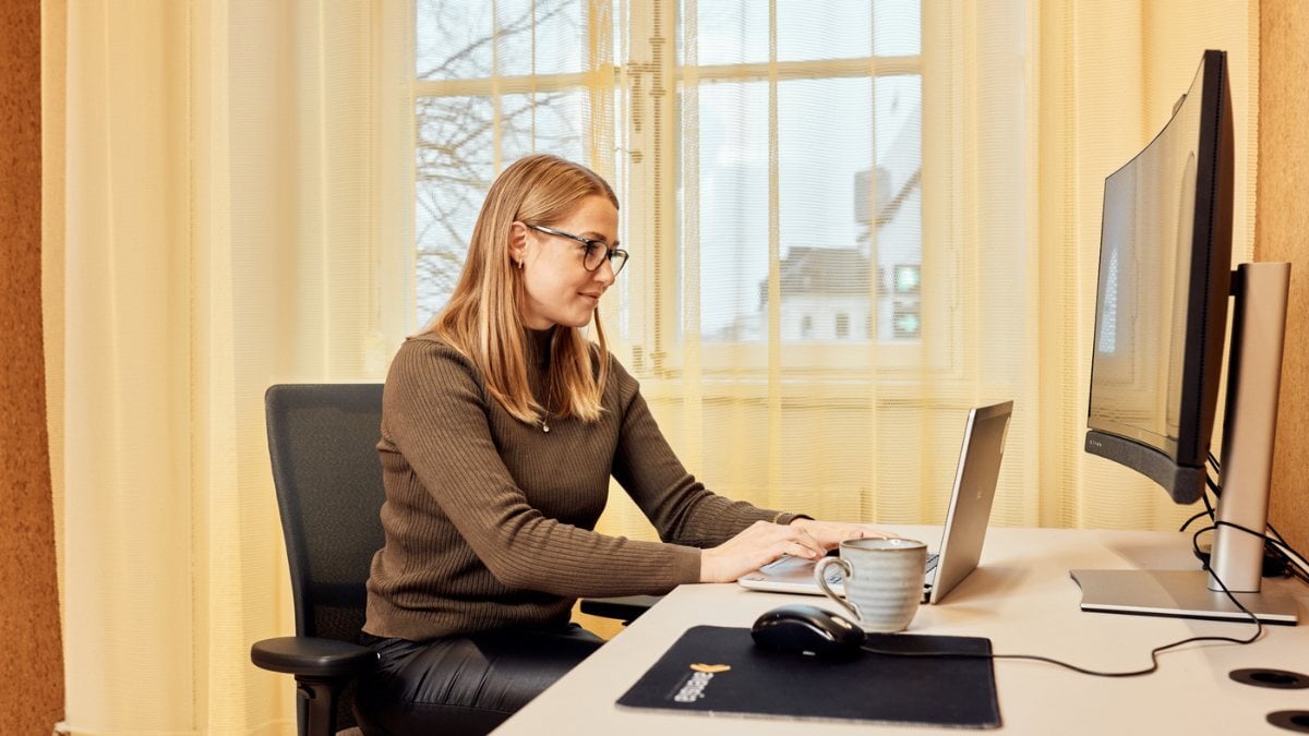 Tjej som sitter och skriver något på sin laptop i ett mötesrum